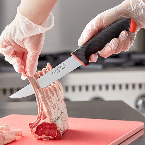 A person in gloves holding a Schraf utility knife with a red handle over a piece of meat on a counter.