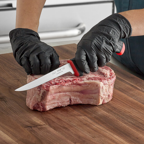A person in black gloves using a Schraf red and black boning knife to cut meat.