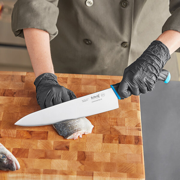 A person in black gloves using a Schraf chef knife to cut fish on a cutting board.