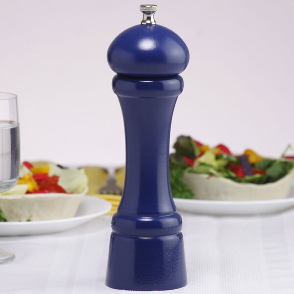 A cobalt blue Chef Specialties salt mill on a table next to a plate of food.