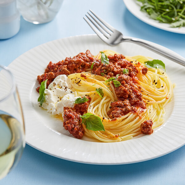 A white plate of Barilla Gluten-Free Spaghetti with meat sauce and cheese next to a fork.