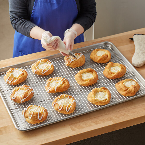 A Baker's Mark stainless steel footed wire cooling rack with pastries with white frosting on it.
