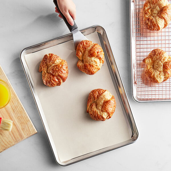 A person using a Baker's Mark PanPal non-stick pan liner to cut croissants on a baking sheet.
