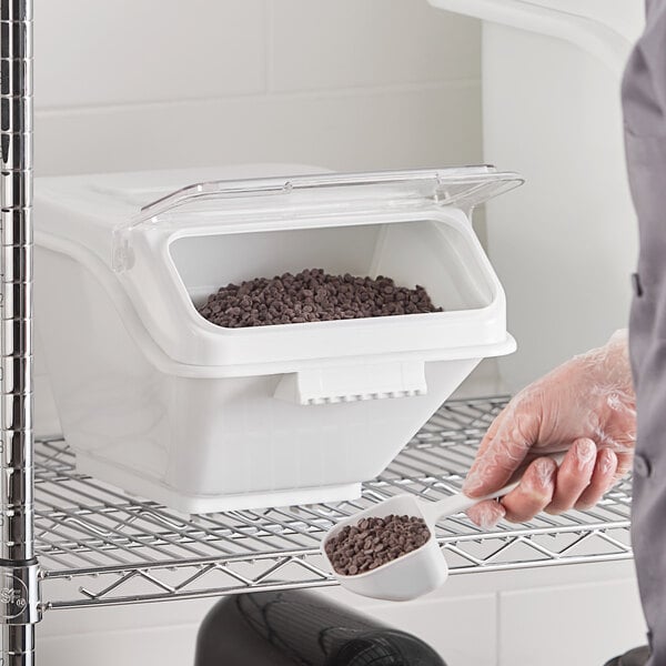 A person using a scoop to measure chocolate powder from a Baker's Mark ingredient bin.