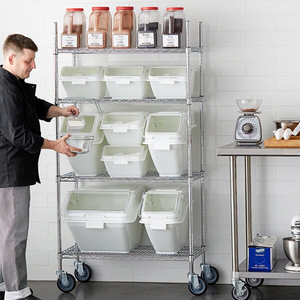 A man standing in front of a shelf with white Baker's Mark ingredient bins with clear lids.