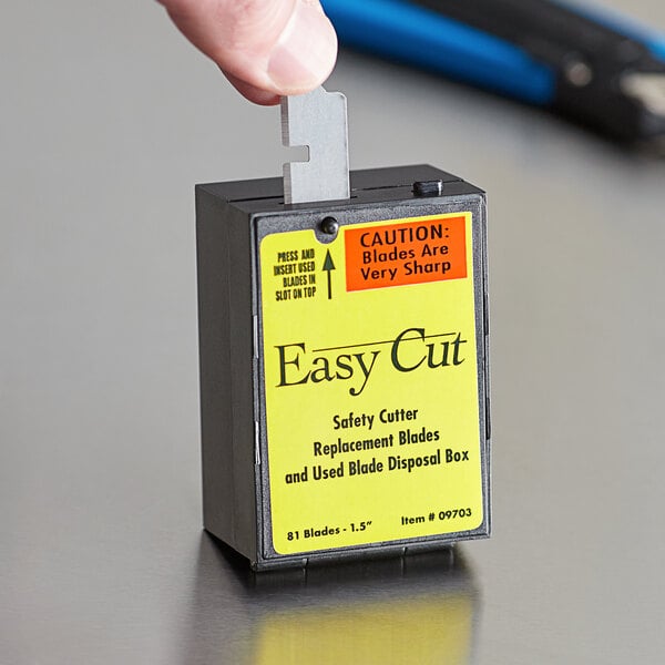 A hand using a yellow and black Garvey safety cutter to cut a box.