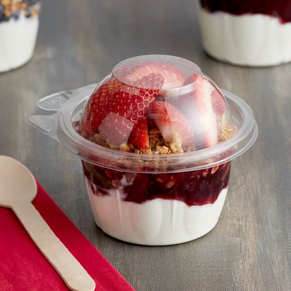 A Dart plastic container of yogurt with strawberries and granola with a dome lid.
