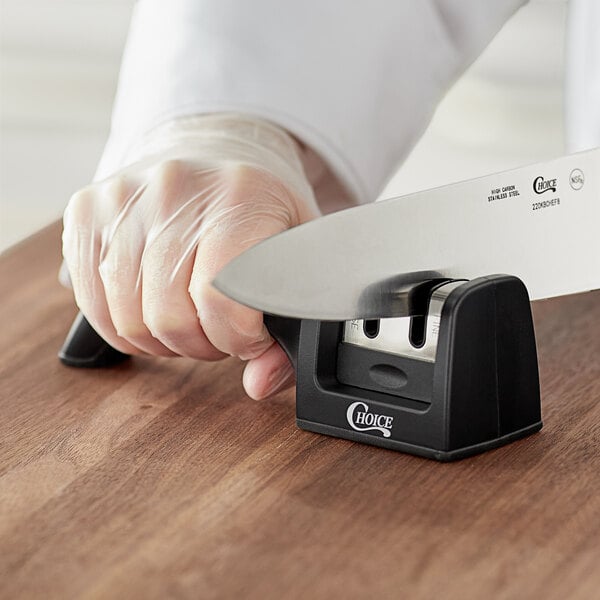 A person holding a Choice handheld knife sharpener and sharpening a knife.