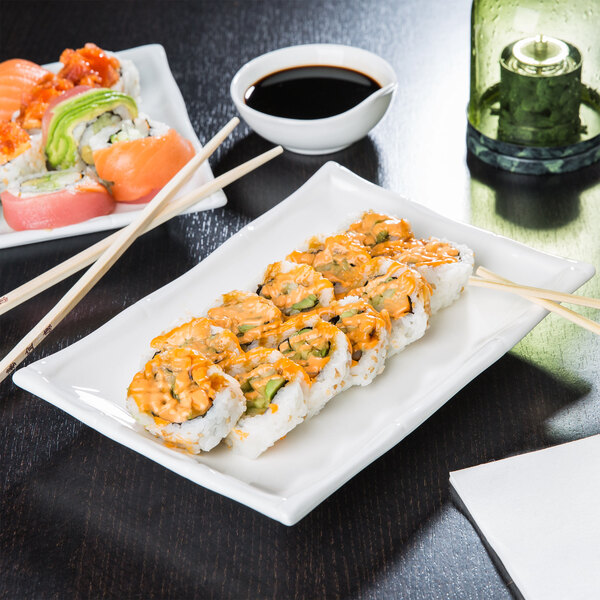 A rectangular white porcelain platter with sushi and chopsticks on a table.
