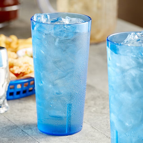 Two blue Choice plastic tumblers filled with ice on a table with a basket of food.