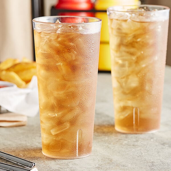 Two Choice clear plastic tumblers filled with iced tea on a table with fries.