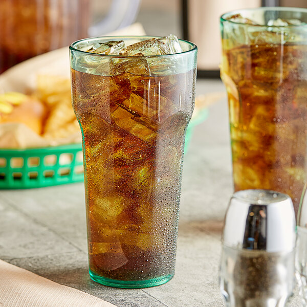 Two Choice green plastic tumblers filled with iced tea and ice on a table.
