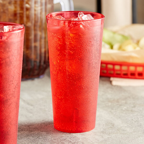 Two red Choice SAN plastic tumblers filled with ice and red liquid on a table.
