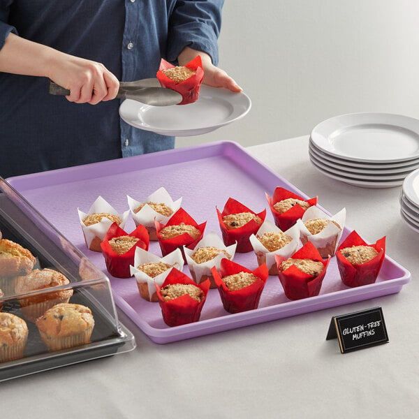 A woman using a purple Choice bakery display tray to serve muffins on a table.