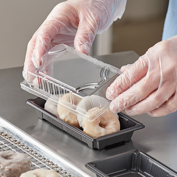 A person in gloves holding a Choice rectangular plastic food container with doughnuts.