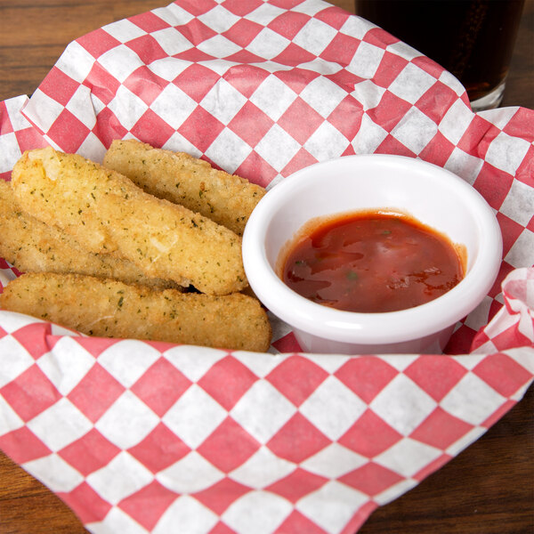 A basket of fried fish sticks with a cup of red sauce.