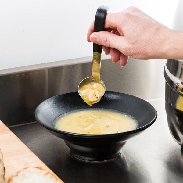 A person using a Vollrath Jacob's Pride stainless steel ladle with a short black handle to spoon soup into a bowl.
