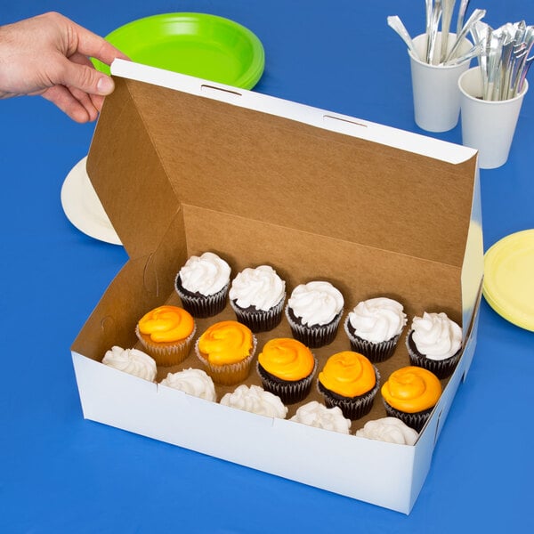 A hand holding a 14" x 10" x 4" white customizable bakery box filled with cupcakes.