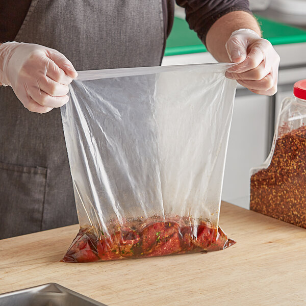 A person in a chef's uniform holding a clear polyethylene layflat bag with food in it.
