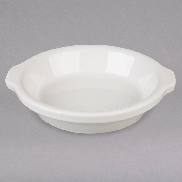 A white Hall China au gratin dish with a handle on a gray surface.