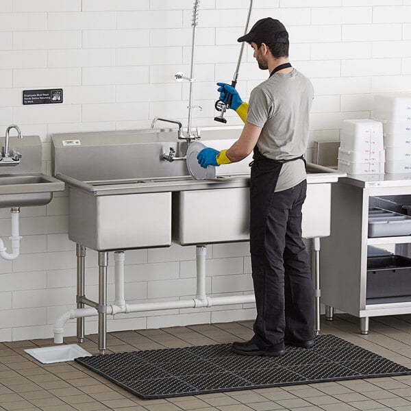 A man wearing gloves and cleaning a Regency 3 compartment stainless steel sink.