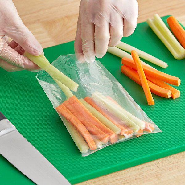 A person's gloved hands cutting a carrot into a clear plastic bag.