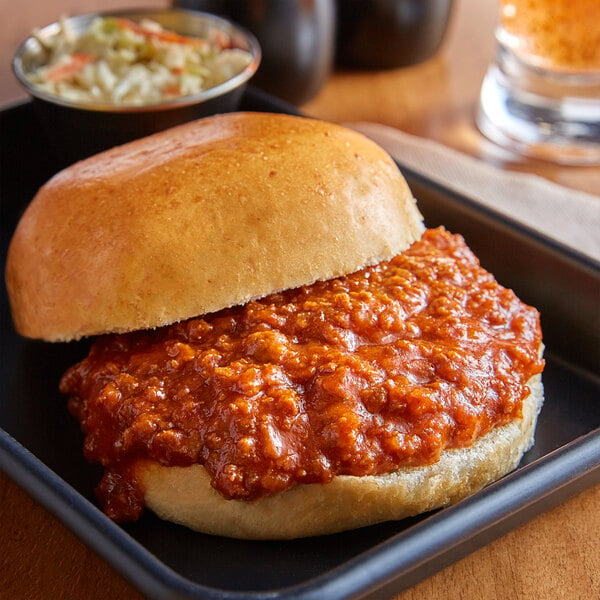 A sandwich with Vanee Beef Sloppy Joe on a table with a bowl of coleslaw.