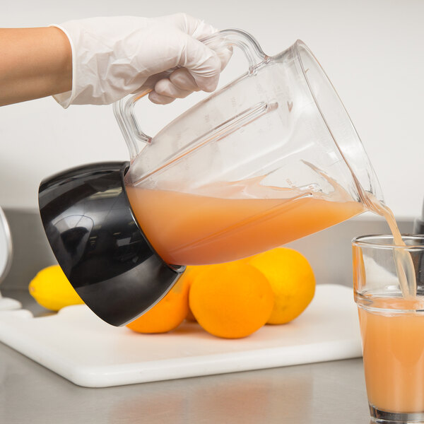 A person pouring orange juice from a Waring blender jar into a glass.