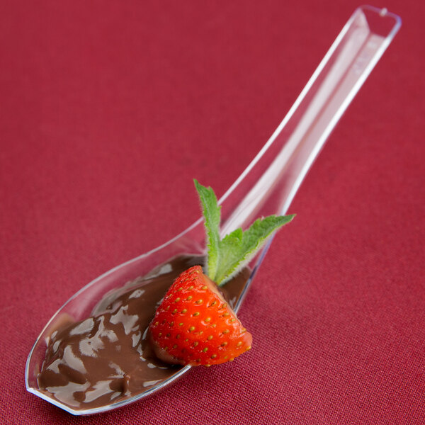 A WNA Comet clear plastic Asian soup spoon with chocolate and strawberry on it.