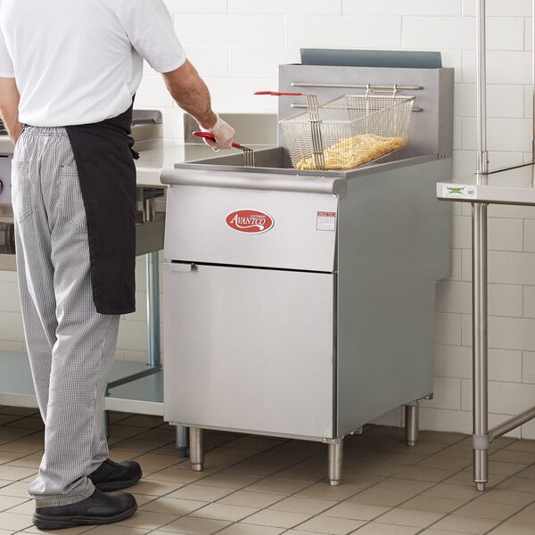 A man cooking food in a commercial kitchen using an Avantco natural gas floor fryer.