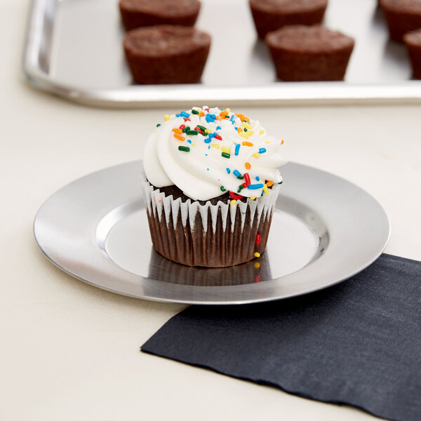 A cupcake with white frosting and sprinkles on a Vollrath stainless steel plate.