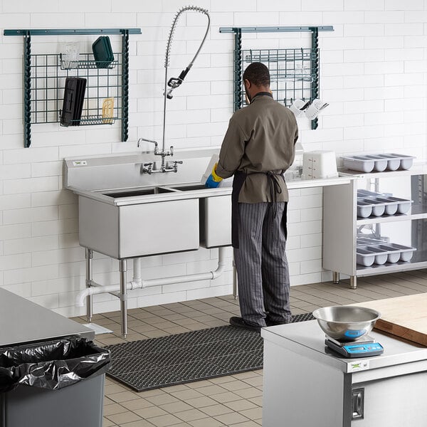 A man standing in a commercial kitchen using a Regency two compartment sink with right drainboard.