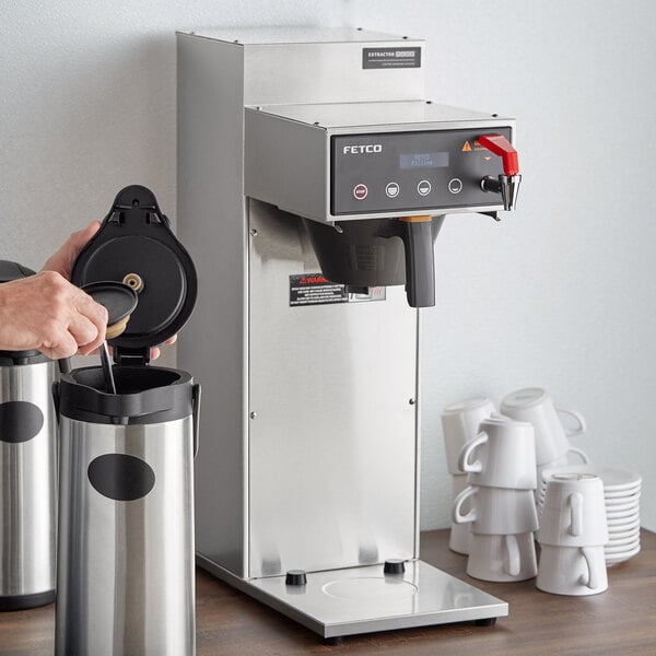 A person using a Fetco airpot coffee brewer to pour coffee.
