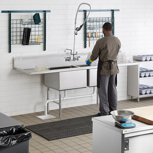 A man using a Regency stainless steel 2 compartment sink with drainboards.