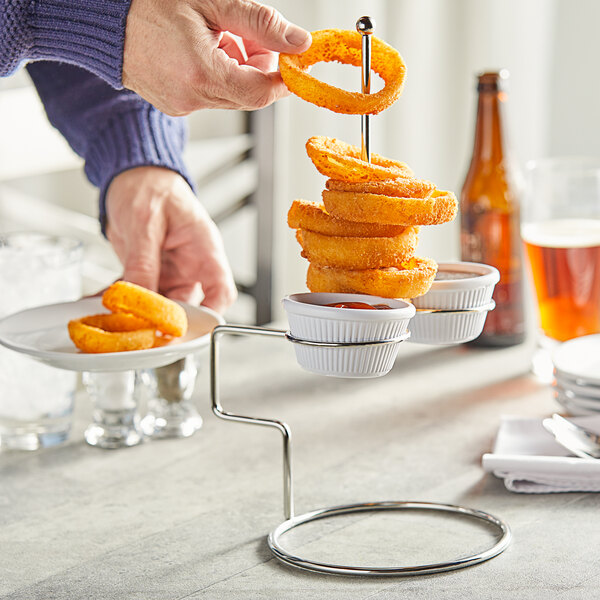 A person holding a Tablecraft stainless steel tower of onion rings with ramekins on a plate.