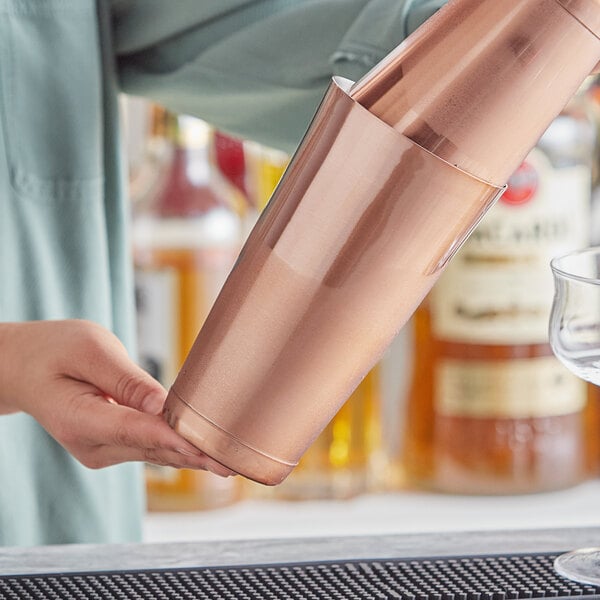 A person using an Acopa copper cocktail shaker to pour a drink.