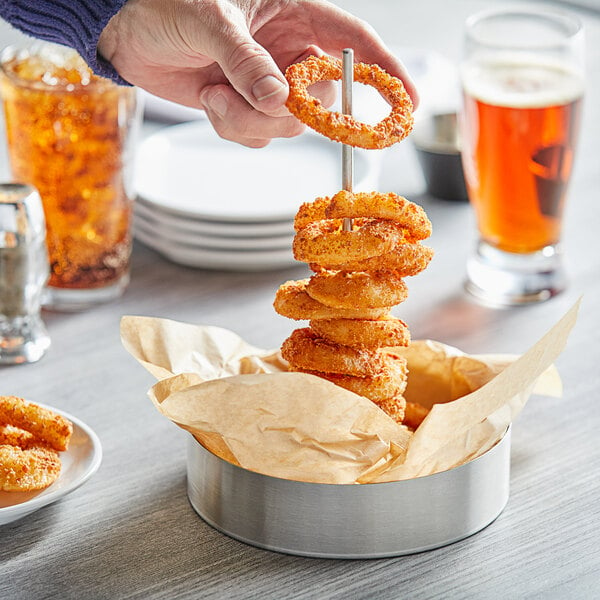 A person holding a Tablecraft stainless steel onion ring serving tower with a stack of fried onion rings.