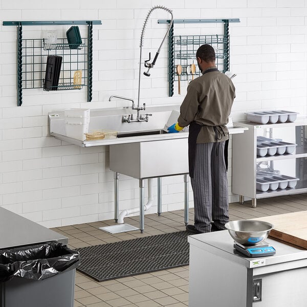 A man standing in a commercial kitchen with a Regency one compartment sink with drainboards.