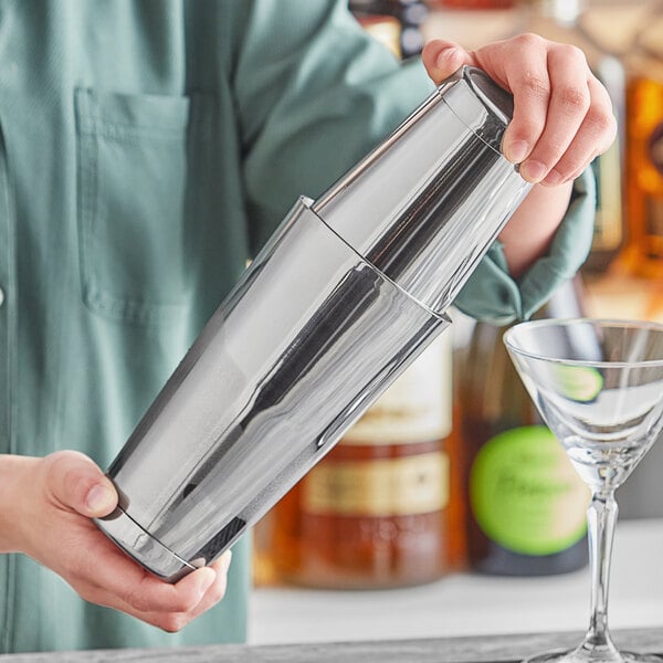 A person holding an Acopa stainless steel cocktail shaker set on a bar counter.