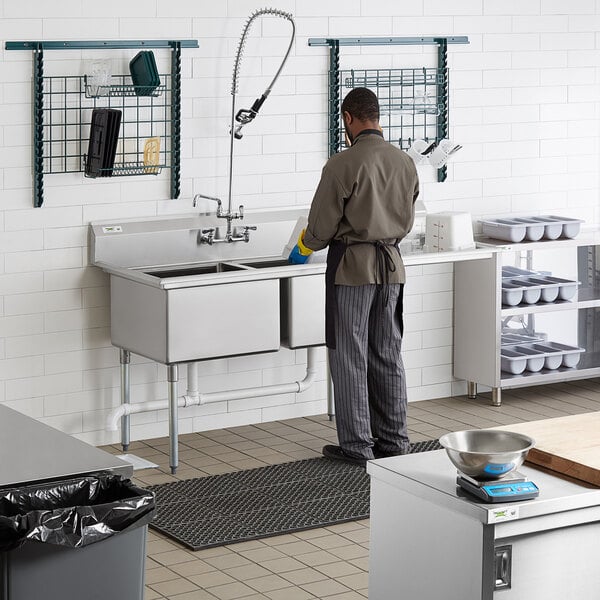 A man washing a Regency two compartment sink in a commercial kitchen.