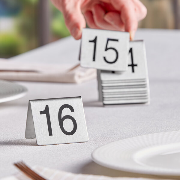 A person holding a Choice stainless steel table number card with the number 3 on it.