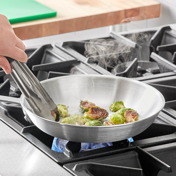 A person cooking brussels sprouts in a Choice aluminum fry pan on a stove.