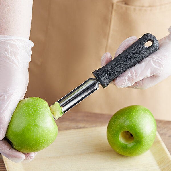 A hand holding a green apple and a black-handled Choice Apple Corer with a hole in the apple.