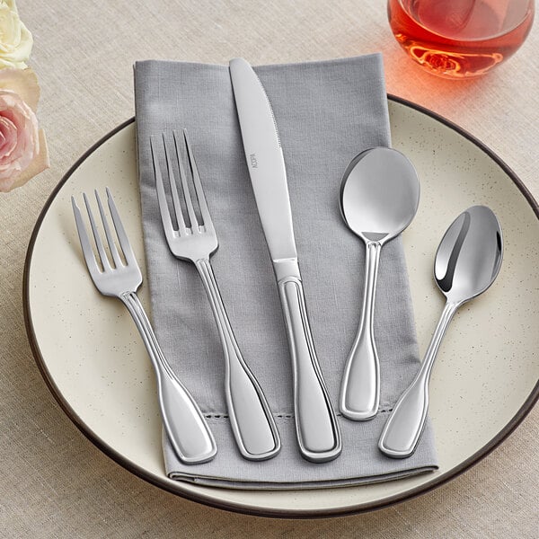 A plate with Acopa Scottdale stainless steel flatware on a grey cloth with a fork and knife.