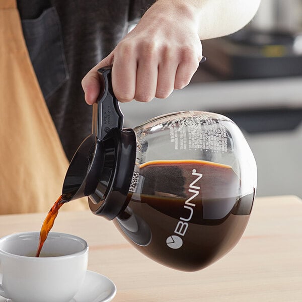 A person pouring coffee into a Bunn glass coffee decanter with a black handle.