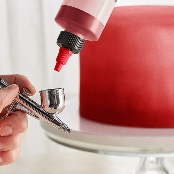 A finger using Chefmaster Metallic Red Airbrush Color to spray a silver object.
