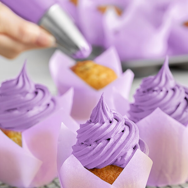 A person using a pastry bag to decorate a cupcake with Chefmaster Neon Brite Purple frosting.