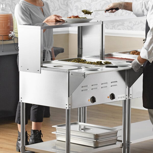 A woman using an Avantco mobile electric steam table in a commercial kitchen.
