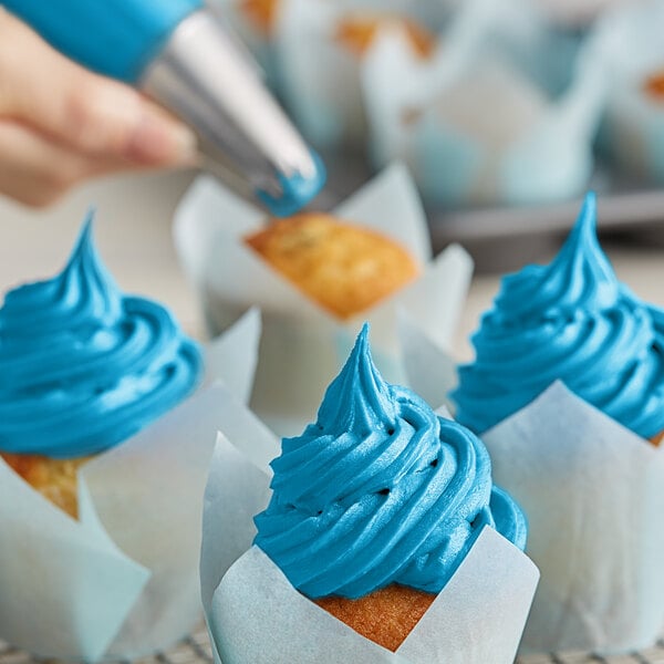 A person using Chefmaster Sky Blue Liqua-Gel to frost cupcakes.