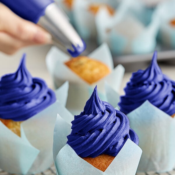 A person using Chefmaster Royal Blue Liqua-Gel to decorate cupcakes with blue frosting.